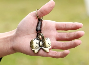 Detailed view of bronze butterfly pendant with brown braided leather keychain held by hand