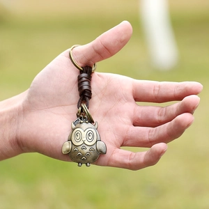 Vintage woven leather keychain with bronze owl pendant held in hand for scale