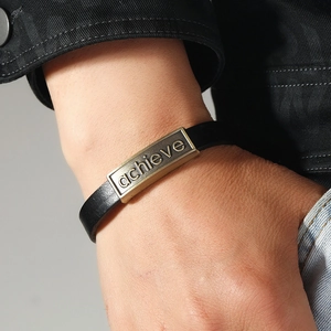 Bracciale unisex in pelle nera con placca 'achieve' in bronzo indossato sul polso