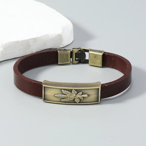 Detail of vintage brown leather bracelet with an engraved bronze maple leaf metal plate