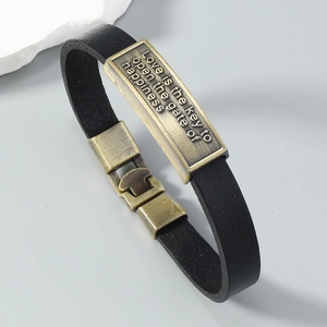 Close-up of vintage leather bracelet with engraved bronze plate showing inspirational text