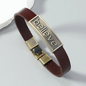 Detail of vintage brown leather bracelet with bronze 'believe' engraved metal plate