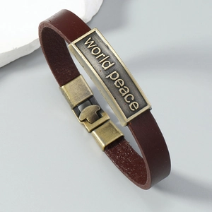 Close-up of World Peace engraved vintage bronze metal plate on a brown leather bracelet