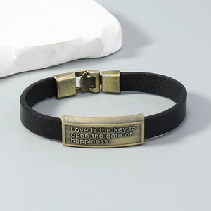 Detail of vintage black leather bracelet with bronze metal plate and engraved quote