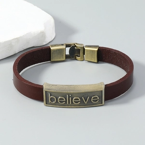 Macro view of vintage brown leather bracelet with bronze 'believe' engraved metal plate