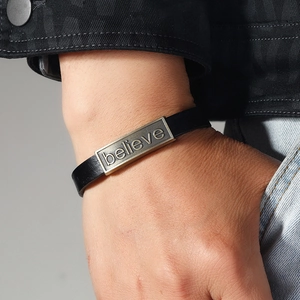 Black leather bracelet with vintage metal plate engraved with believe on a wrist