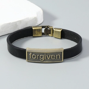 Détail du bracelet en cuir noir avec plaque en bronze vintage et gravure forgiven