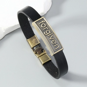 Détail d'un bracelet vintage en cuir noir avec plaque en bronze gravée forgiven