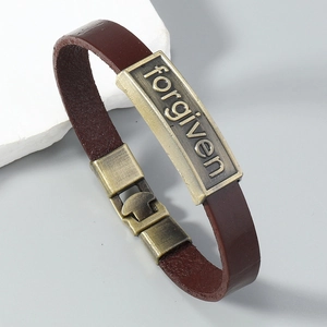 Détail d'un bracelet vintage en cuir marron avec plaque en bronze antique et gravure forgiven