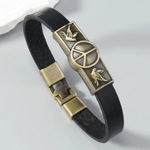 Detail of vintage black leather bracelet with bronze peace sign and bird engraving buckle