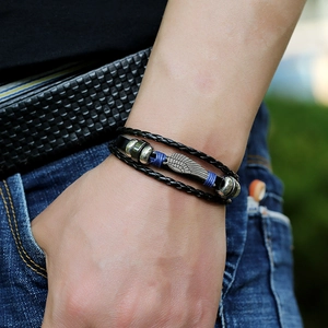 Detail of multilayer leather bracelet with silver wing pendant and blue thread wrap