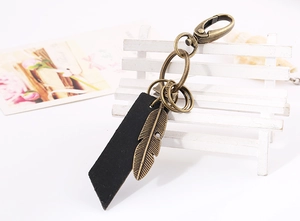 Detailed close-up of retro leather keychain with bronze feather pendant and metal lobster clasp
