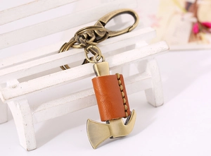 Detail of bronze hammer keychain with orange leather cover on mini white bench