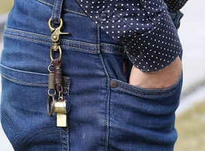 Detail of vintage brass whistle keychain with leather wrap hooked on denim jeans loop