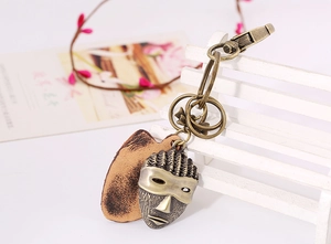 Detail of vintage bronze mask keychain on a white bench with leather and metal accents