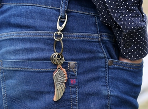 Detail of vintage bronze wing keychain with leather backing on blue jeans belt loop