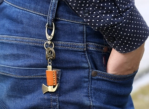 Detail of vintage bronze axe keychain with leather case hanging on denim jeans