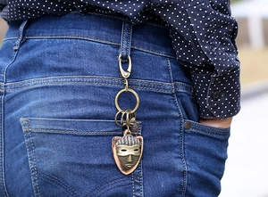 Detail of a vintage bronze mask keychain clipped to blue denim jeans with a metal clasp