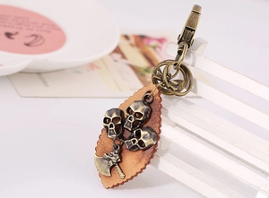 Detail of vintage bronze skull charms on brown leather leaf keychain with spring clasp