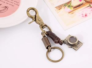 Detailed view of a vintage alloy camera pendant with a retro brown leather keychain strap