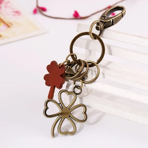 Vintage bronze four-leaf clover keychain with red leather accent on white wooden fence