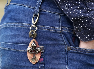 Detail of vintage punk skull keychain with leather backing and mini axe pendant on denim