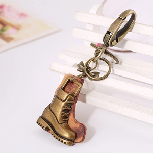 Vintage bronze boot keychain with leather sole and metal bow on a white bench