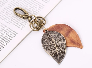 Detail view of retro bronze leaf and leather keychain against a soft book background