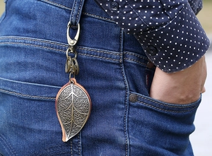 Macro view of bronze leaf keychain with leather backing on blue denim jeans loop
