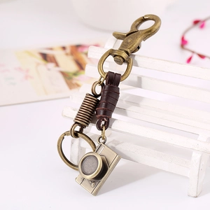 Vintage leather camera keychain with bronze metal hook on a decorative white wooden chair