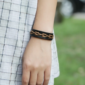 Détail d'un bracelet en cuir de vachette tressé noir et marron porté au poignet