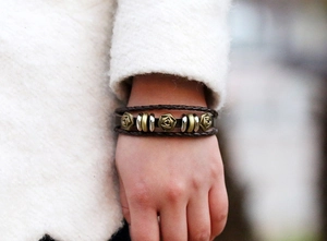 Detailed close-up of woven leather bracelet with vintage metal rose charms and beads