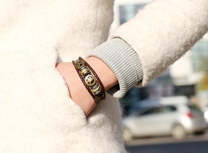 Macro shot of multi-layer leather bracelet featuring peace sign charm and bronze beads