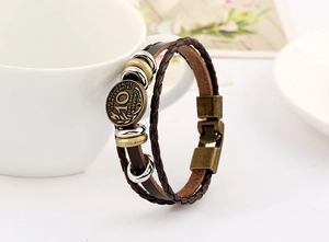 Detail of vintage braided leather bracelet with engraved coin and metal clasps