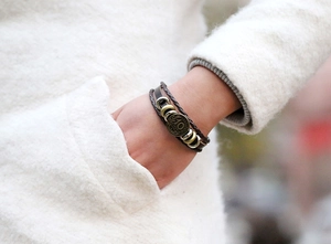 Macro shot of multi-layer braided leather bracelet with vintage coin on wool coat