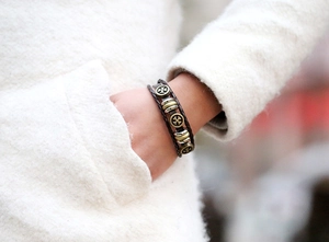 Close-up of multilayer braided leather bracelet with vintage bronze cross charm on wrist