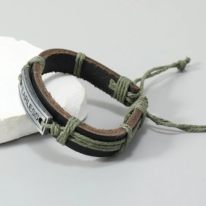 Detail of woven brown leather bracelet with silver Fearless charm on white rocks