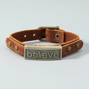 Close-up of brown leather punk bracelet with engraved believe metal plate and rivets