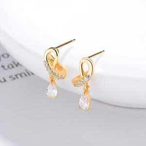Gold-plated silver crossover earrings with pear-cut zircon pendants on white ceramic