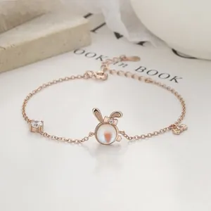 Macro detail of rose gold bunny pendant with moonstone and carrot inlay on dainty bracelet