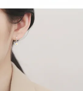 Detailed view of sterling silver daisy charm hoop earrings worn by a model in soft light