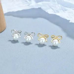 Detailed view of silver and gold bowknot pearl earrings with zircon stones on blue texture