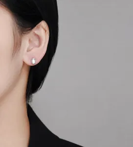 Detailed close-up of an oval moonstone stud earring with silver threaded texture on ear