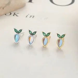 Macro view of carrot-shaped moonstone earrings with emerald leaves in silver and gold