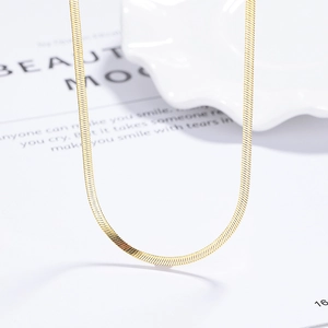 Elegant gold flat snake chain necklace on white textured tray with fashion magazine style