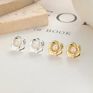 Macro view of gold and silver camellia flower stud earrings with central pearl inlay
