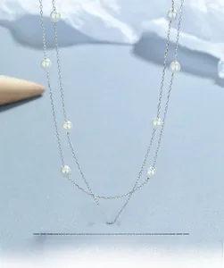 Detailed view of double-layer silver necklace featuring round white pearls on a light blue background