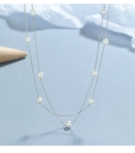 Detail of double-layer silver station necklace with white pearls on a blue surface