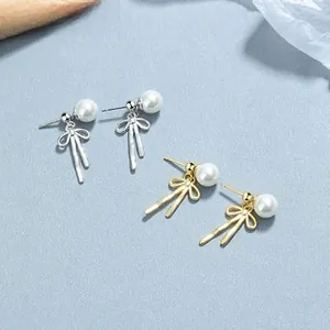 Close-up of 925 silver and gold butterfly pearl stud earrings on a blue textured background