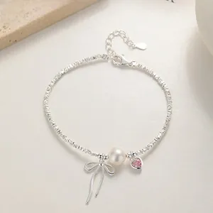 Detail of 925 silver bracelet featuring pearl, pink heart gem and bow pendant